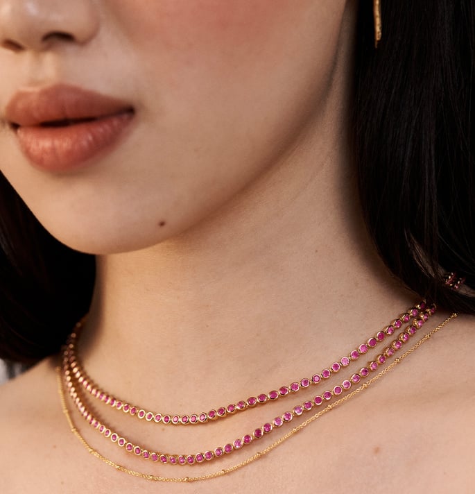 A model wearing two Gemstone Tennis Necklaces with Pink Quartz, and a beaded chain necklace